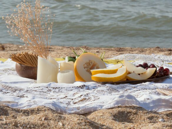 Beautiful summer picnic on the beach at sunset in boho style. Organic fresh fruit on linen blanket. Vegetarian eco idea for weekend picnic.