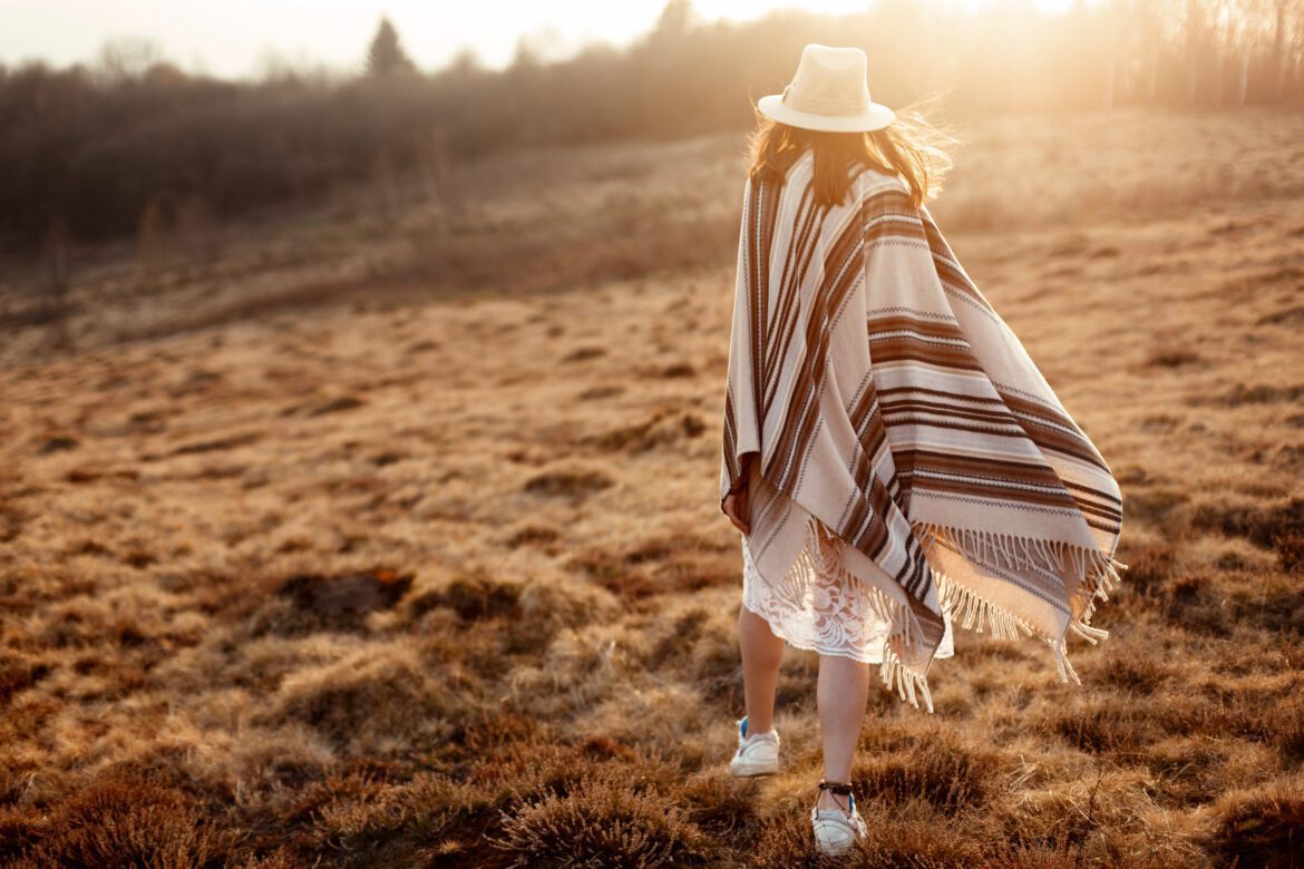 happy boho woman, walking towards sun, wearing hat and poncho at