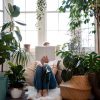 Young girl sitting by a window with houseplants reading a book covering her face