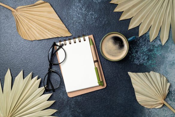 Notebook, coffee cup, dried palm leaves decor on desk of home office flat lay. Freelance, blogging, feminine, working concept top view. Copy space
